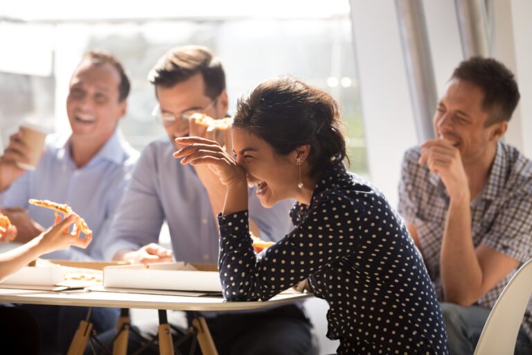 Indian woman laughing eating pizza with diverse coworkers in off
